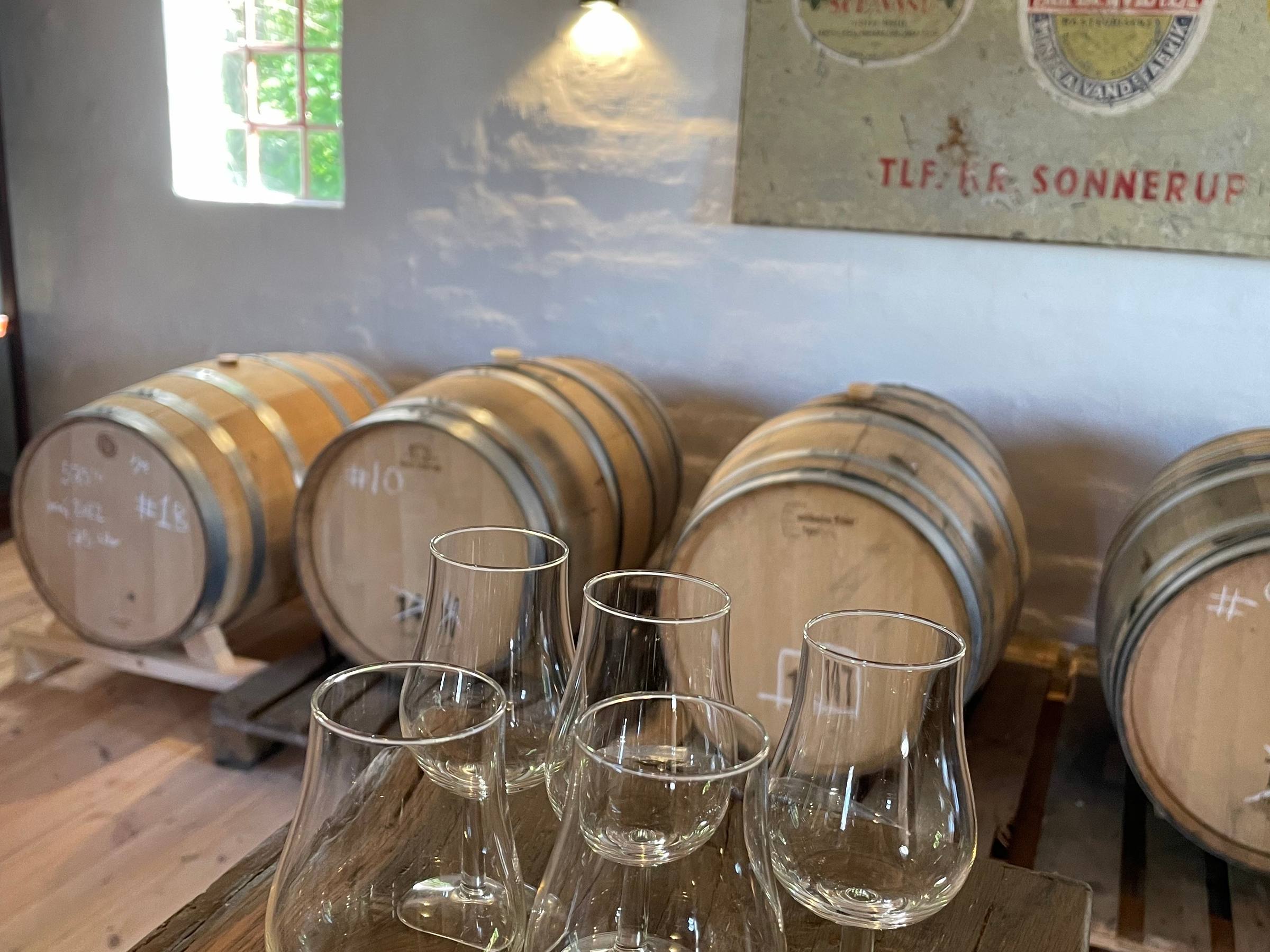 Det gamle emaljeskilt for Vintre Mølle Bryggeri & Mineralvandsfabrik på væggen i fadrummet, over fade og en række glas.